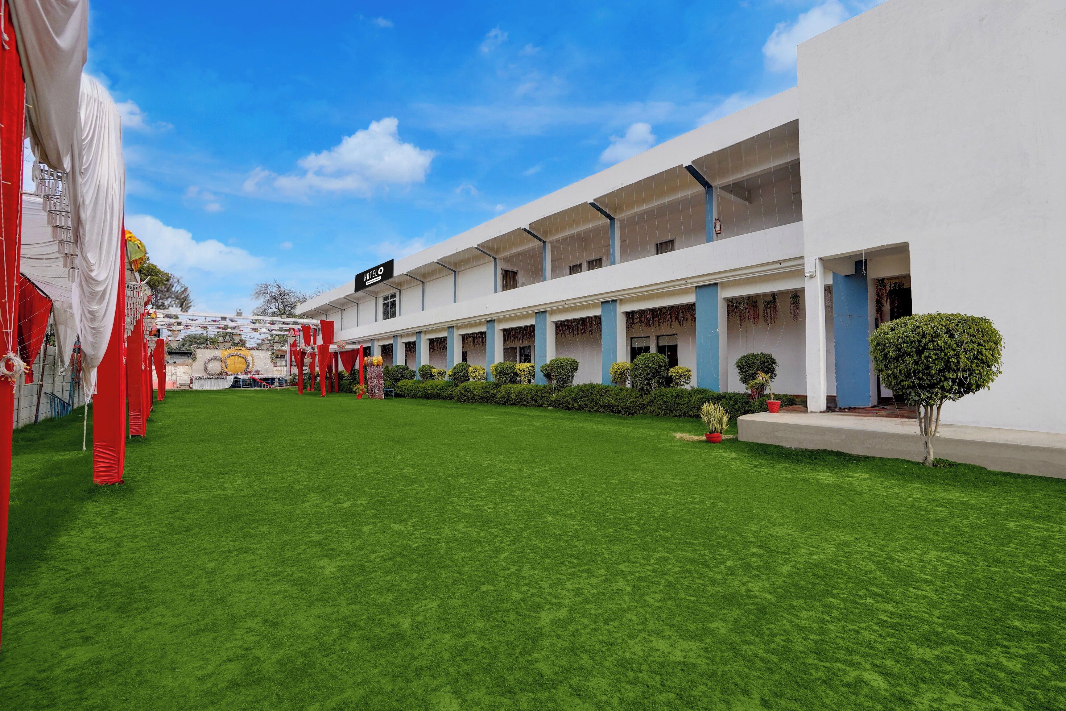 Un hotel con un área exterior cubierta, césped y un edificio con un cartel que dice 'HOTEL'.