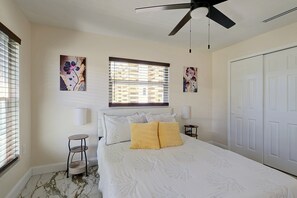 Ein Schlafzimmer mit einem Bett, einer Stehlampe, einem Deckenventilator und Kunstwerken an den Wänden.
