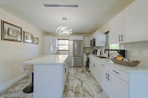 A modern kitchen with white cabinetry, a marble floor, and a central island. - Right on Canal! Sleek Home Near Gulf Coast Fun (Hudson)