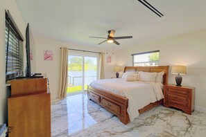 A bedroom with a bed, nightstands, a ceiling fan, and a view of a lake through the window. - Right on Canal! Sleek Home Near Gulf Coast Fun (Hudson)