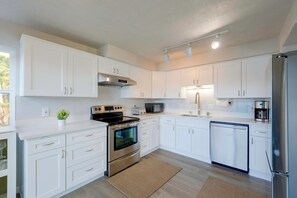 A modern kitchen with white cabinetry, stainless steel appliances, and a visible clock on the wall. - Deception Pass Waterfront: Salish Sea Serenity (Anacortes)