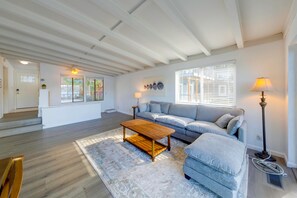 A spacious living room with a wooden coffee table, a grey sofa, and a large window with blinds. - Deception Pass Waterfront: Salish Sea Serenity (Anacortes)