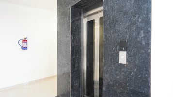 Un ascenseur moderne avec un mur en marbre, un extincteur fixé au mur et un panneau de commande également fixé au mur.