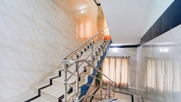 Uma escadaria moderna com corrimão de metal, paredes de mármore e um vaso de planta.