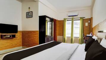 A hotel room with a bed, a TV, a wardrobe, and a window with curtains.