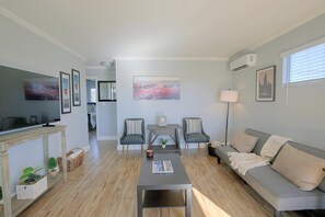 A modern living room with a flat-screen TV, a grey sofa, a coffee table, and a dining area with chairs. - Chic Apt < 5 Mi to SDSU! Private Patio & Views (La Mesa)