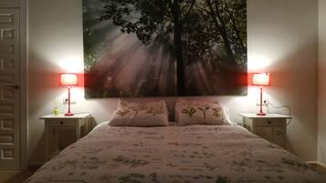 Un dormitorio con una cama, dos mesitas de noche, dos lámparas y un cuadro grande en la pared de un árbol con luz solar.