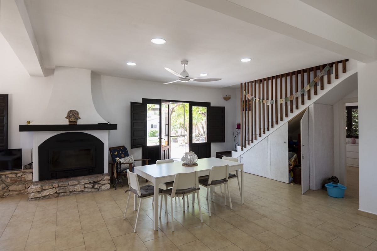 Amplia sala de estar con chimenea, mesa de comedor y escalera que conduce a un nivel superior.