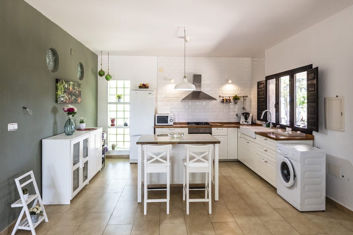 A modern kitchen with white cabinetry, a central island, a built-in washing machine, and a dining area with two chairs.
