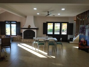 A spacious living room with a fireplace, a dining area with chairs, and large windows with shutters. - New Listing (Bullas)