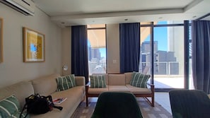 A hotel room with a sofa set, a chair, a framed picture on the wall, and a view of the city through large windows. - Manhattan Feeling! 2BR, Huge Terrace & Epic Views, 2min walk Bree Street (Cape Town)