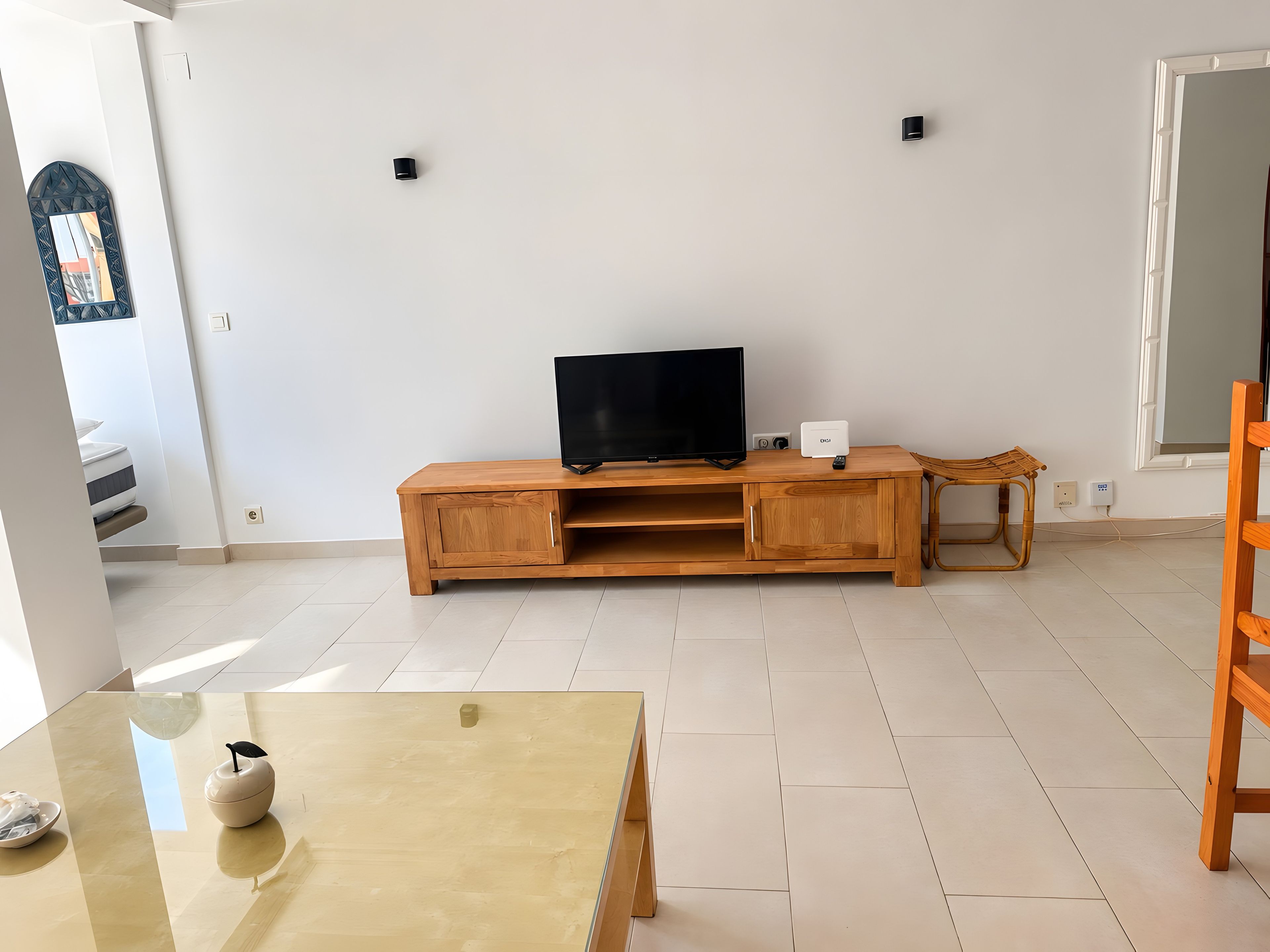 Un salón minimalista con un mueble de madera para entretenimiento, un televisor, una mesita con un florero y un ventanal.