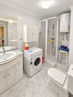 Een moderne badkamer met een ingebouwde wasmachine, een douchecabine en een toilet.
