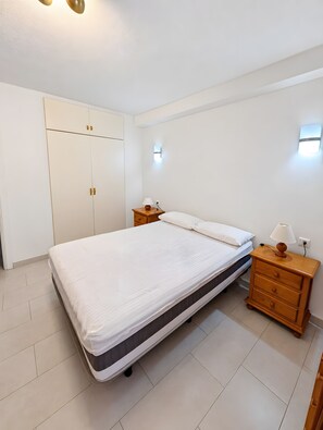 Een slaapkamer met een bed, een kledingkast, een nachtkastje en een wandlamp.