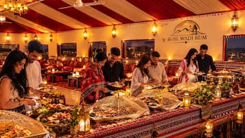 A banquet hall with a long table set for a meal, a ceiling fan, and a wall with the name 'ROSE WADI ROM'.