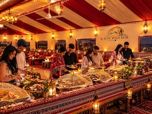 En festlokal med ett långt bord dukat för en måltid, en takfläkt och en vägg där namnet ”ROSE WADI ROM” står.