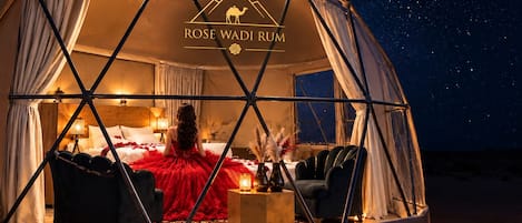 A dome-shaped tent with a bed, a red dress, and a night sky view.