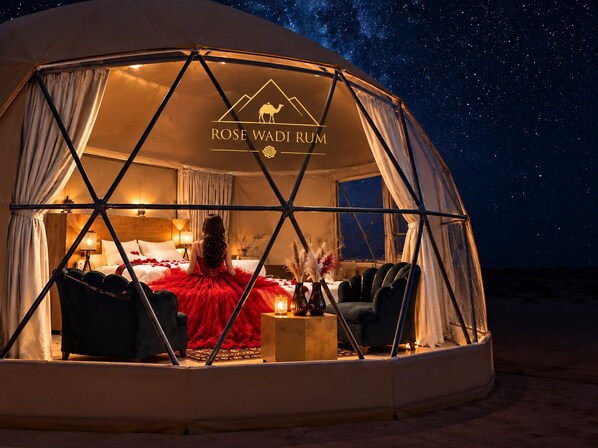 A dome-shaped tent with a bed, a red dress, and a night sky view.