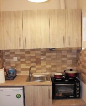 Une cuisine avec des meubles de rangement en bois, un pare-feu en carrelage, un évier, un four à micro-ondes et un petit réfrigérateur.