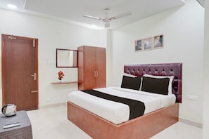 A bedroom with a bed, a wardrobe, a mirror, a ceiling fan, and a small shelf with flowers. - Super Hotel O Magunta Layout Nellore (Nellore)