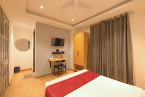A bedroom with a bed, a desk, a chair, a wardrobe, a television, and a ceiling fan. - Hotel Capital Leaf (New Delhi)