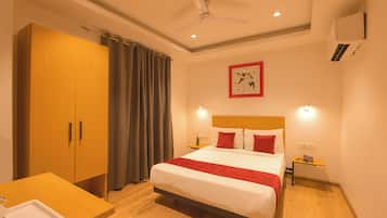 Une chambre d’hôtel comprenant un lit, une armoire en bois, un bureau avec un plateau, un ventilateur de plafond, une œuvre d’art accrochée au mur et une table de chevet avec une lampe.