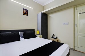 Una habitación de hotel con cama, mesita de noche, lámpara, un cuadro y una puerta.