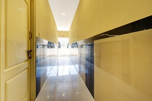 Um corredor com piso refletivo, uma porta à esquerda e uma parede com padrão em preto e branco à direita.