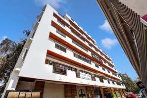 Um edifício de vários andares com fachada branca, diversas varandas e uma placa com a inscrição Sai Siri Medicals & General Store.