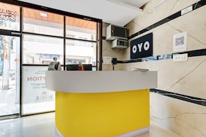 En receptionsdisk med gul bund og hvid overflade, en vægmonteret klimaanlæg og et skilt med 'OYO' branding.
