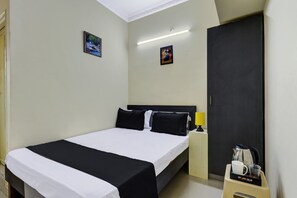 Quarto de hotel com cama, mesa de cabeceira, abajur e cafeteira.