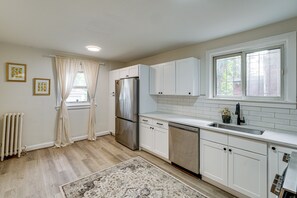 A kitchen with white cabinets, a stainless steel refrigerator, a dishwasher, and a window with curtains. - Historic Detroit Charm Near Area Hospitals (Detroit)