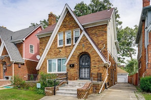 A two-story brick house with a gabled roof, a front door with decorative ironwork, and a small front porch with steps. - Historic Detroit Charm Near Area Hospitals (Detroit)