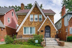 A two-story brick house with a gabled roof, a front door with a decorative iron gate, and a small front yard with a sign for the Marygrove Community Association. - Historic Detroit Charm Near Area Hospitals (Detroit)