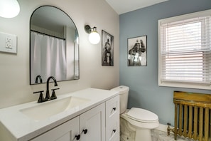 A bathroom with a white sink, a mirror, a toilet, and a window with blinds. - Historic Detroit Charm Near Area Hospitals (Detroit)