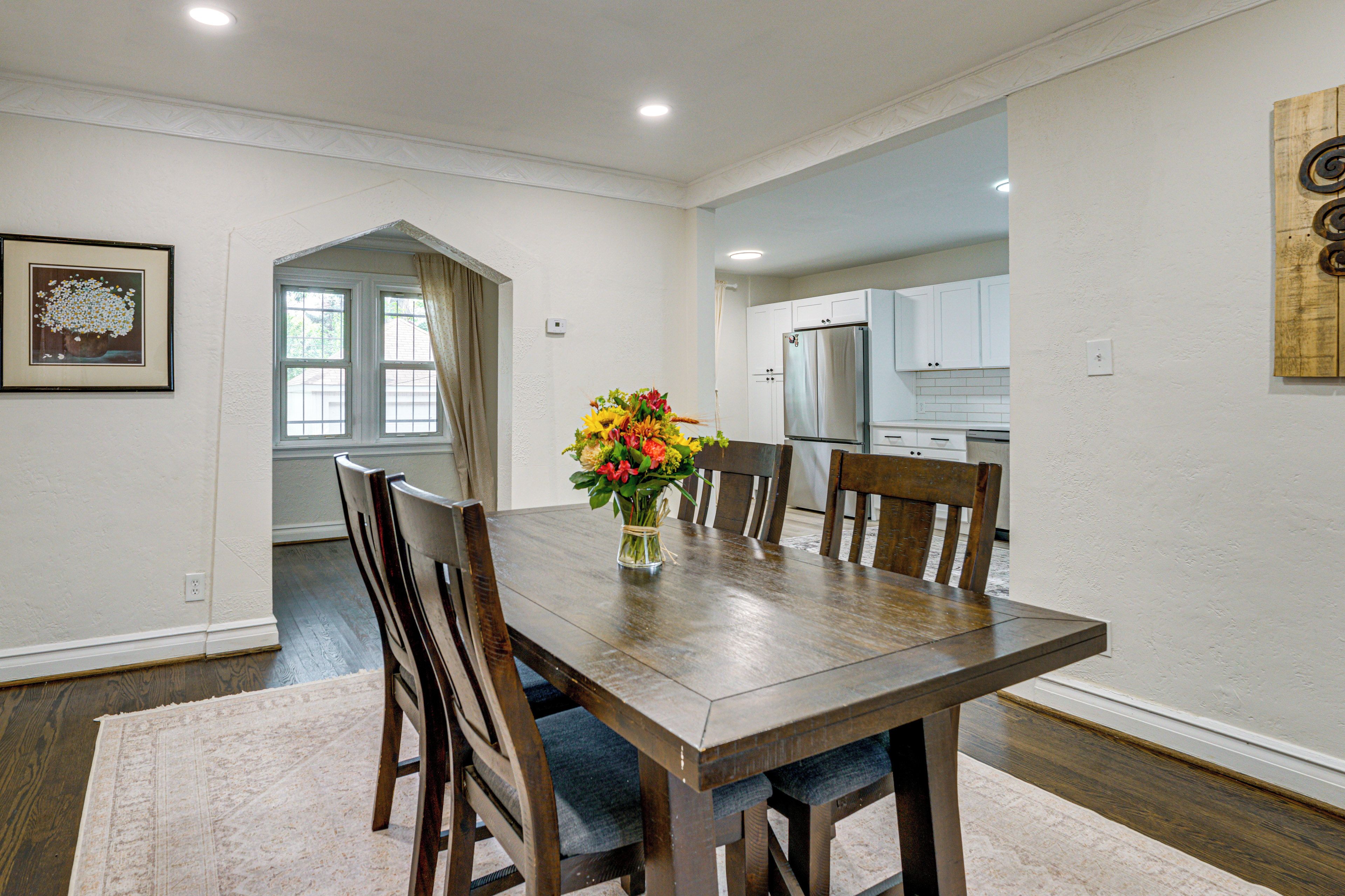 A dining area with a wooden table, chairs, and a vase of flowers.
