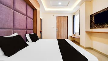 Een hotelkamer met een groot bed, een houten hoofdbord, een flatscreen televisie aan de muur en een houten deur.