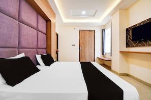 A hotel room with a large bed, a wooden headboard, a flat-screen TV mounted on the wall, and a wooden door. - OYO 835663 Hotel Drishti Grand (Lucknow)