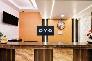 Una recepción con un letrero que dice 'OYO', un reloj en la pared, una cámara de seguridad y una estatua de Buda.