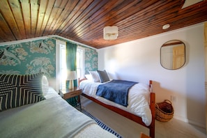 Una camera da letto con due letti, un soffitto in legno, una finestra con tende, un comodino con una lampada e uno specchio a parete.