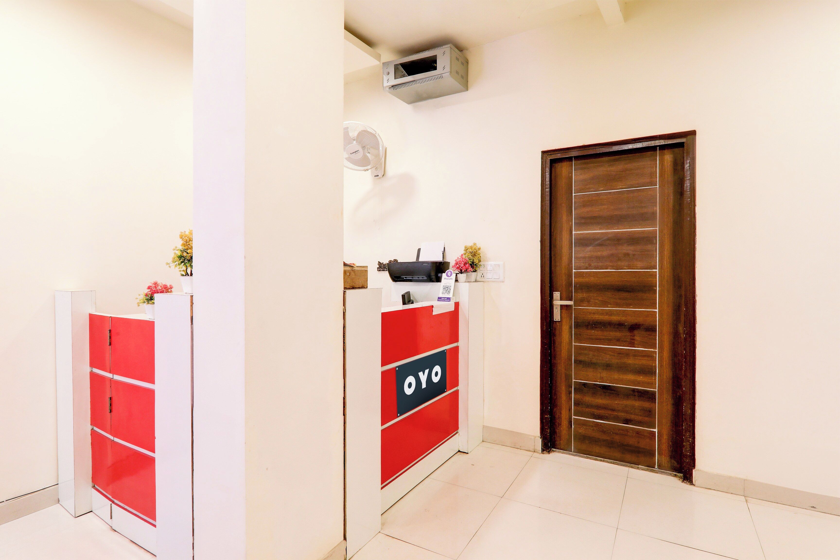 Un área de recepción con un mostrador rojo y blanco, una puerta de madera y una unidad de aire acondicionado instalada en el techo.