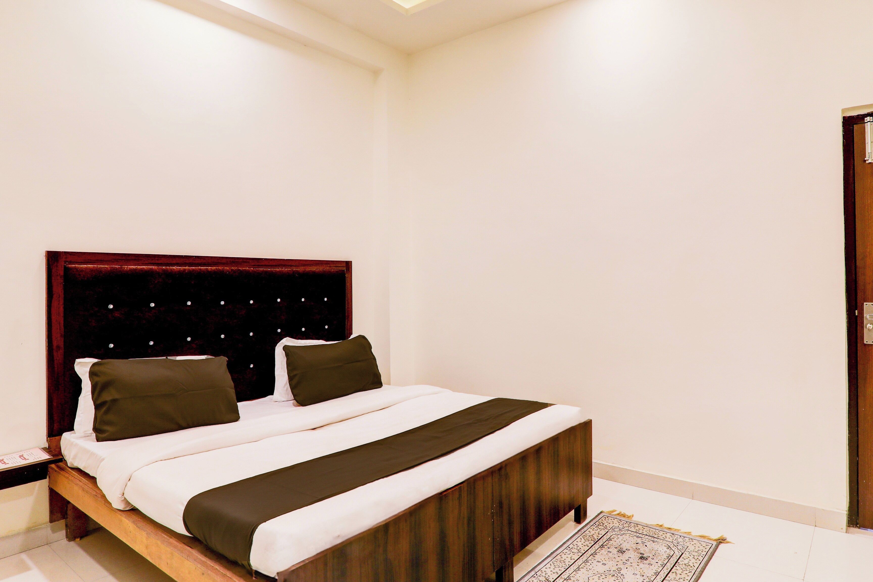 Un dormitorio con cama, cabecera de madera y alfombra estampada.