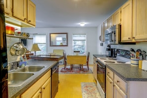 A kitchen with wooden cabinets, a stove, a microwave, and a dining area with a table and chairs. - Saint Albans Home: Walk to Main Street! (Saint Albans City)