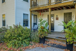 A two-story house with a porch, a front door, and a small garden area with plants and fallen leaves. - Saint Albans Home: Walk to Main Street! (Saint Albans City)