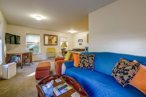 A living room with a blue sofa, a wooden coffee table, a TV, and a dining area with a table and chairs. - Saint Albans Home: Walk to Main Street! (Saint Albans City)