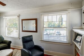 A room with a black leather chair, a white-framed mirror, and a view of the street through large windows with blinds. - Walk to Pickleball, Parks, Pubs! Cozy Dtwn Apt (Bakersfield)