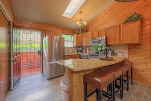 A kitchen with wooden cabinets, stainless steel appliances, a granite countertop, and a bar stool area. - Walk to Midtown! Family Getaway w/ Wraparound Deck (Ruidoso)
