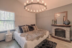 A bedroom with a bed, a fireplace, a chandelier, and a window with blinds. - Walk to Midtown! Family Getaway w/ Wraparound Deck (Ruidoso)