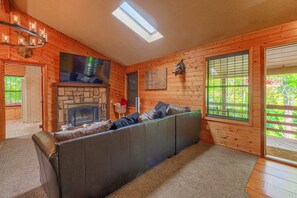 Ein rustikales Blockhaus-Interieur mit Kamin aus Stein, einer Couch und einem großen Fenster.