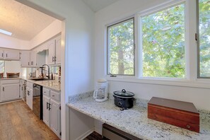 A kitchen with white cabinetry, a granite countertop, a coffee maker, a slow cooker, and a window with a view of trees. - Lake Hartwell Home w/ Quiet Patio & Lake Access (Townville)